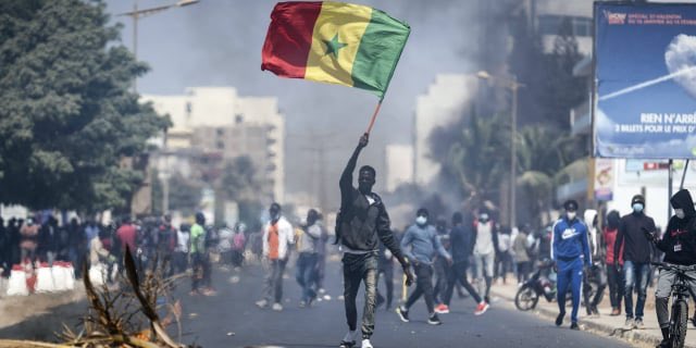 Keterangan Foto: Salah satu pengunjuk rasa mengibarkan bendera Senegal ketika protes. Sumber foto: Twitter @bashou_sn