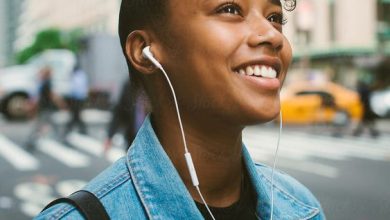 Happy young woman listening to headphones in city street, smiling and wearing jean jacket and looking up with skyscrapers behind her. Sumber Foto: Pinterest